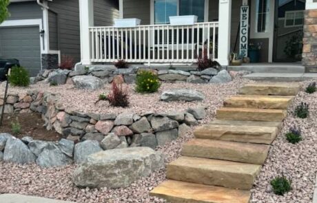 Front yard with stone steps, rock garden, and a porch with white railing and a "Welcome" sign.