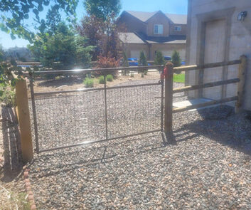 A metal gate on a gravel path with some trees and a house in the background.