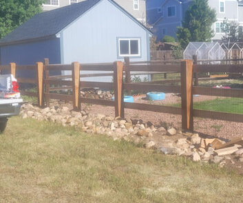 A wooden fence borders a backyard garden with a small shed, gravel path, and a blue kiddie pool. Houses are visible in the background.