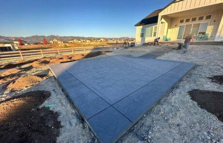 Newly constructed concrete patio in a backyard, with a house on the right and open landscape in the background.